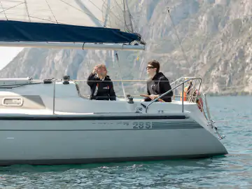 Zwei Segler im Cockpit eines Segelboots vor den Bergen am Gardasee